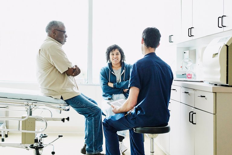 Senior male patient and adult daughter consulting with male nurse during check up in exam room