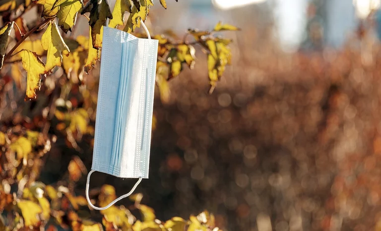 medical mask hangs against the background of blurred autumn foliage